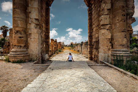 Happy Woman Enjoying Beauty and Majesty of the High Columns and Arches of Ruins of Tire. Excursion in Necropolis. Lebanon. Discovering the World. Active Summer Vacation.の写真素材