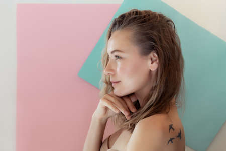 Profile Portrait of a Beautiful Young Woman with Birds Tattoo on the Shoulders. Gentle Pastel Colors Background. Authentic Beauty of Young Woman.の写真素材