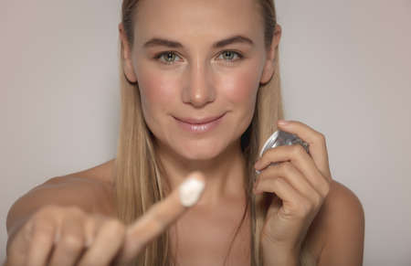 Portrait of a Pretty Woman Isolated on a Beige Background Applying Face Cream. Young and Fresh Face. Beauty and Health Conceptの写真素材