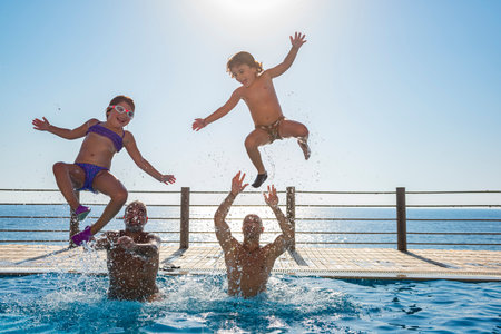 Two Happy Kids with Their Fathers Having Fun in the Pool. Jumping and Making Splashes. Enjoying Summer Holidays on the Beach Resort.の写真素材