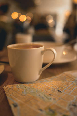 Closeup Photo of a Cup of Coffee near Map in Little Cozy Caffe. Tourists Searching the Right...