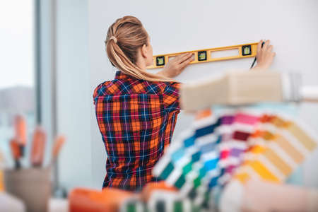 Pretty Woman Doing Repair With Level Ruler near the Wall. Choosing New Colors For Apartment. Professional at Work.の写真素材