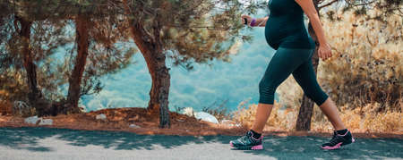 Sportive Pregnant Woman Jogging in the Mountainous Forest in Sunny Day. Enjoying the Walk Among...