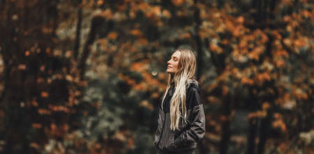 Nice Blond Woman With Closed Eyes Enjoying Beautiful Autumn Nature in the Park. Pretty Girl over Blurry Autumnal Foliage Background.の写真素材