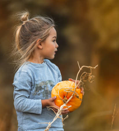 Portrait of a Cute Little Boy with a Pumpkin in the Garden. Food and Decoration For Thanksgiving and Halloween Holidays. Autumn Harvest Season.の写真素材