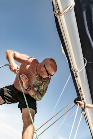 Portrait of a Handsome Man Working on Sailboat. Pulls the Rope. Summer Holidays on Water Transport....