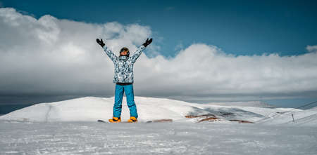 Active Woman with Raised Up Hands Standing on Snowboard in High Snowy Mountains. Spending Winter Vacation on Ski Resort. Happy Sportive Lifestyle.の写真素材