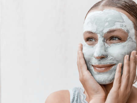 Portrait of a Beautiful Young Woman Applying Clay Mask Isolated on White Background. Enjoying Day Spa in Beauty Clinic.の写真素材