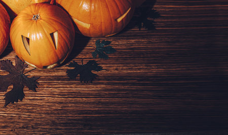 Beautiful Stylish Halloween Still Life on Wooden Background. Carved Jack-o-lanterns Decoration with Dry Maple Leaves. Happy Halloween Party.の写真素材