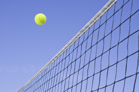 Yellow Tennis Ball Flying Over the Net Against a Clear Blue Sky