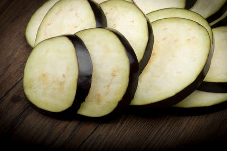 Aubergines eggplants and slices on wood backgroundの写真素材