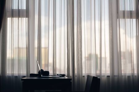 a notebook put on the wood table beside of the large window with curtain with nobody in the room of...