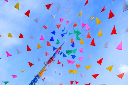 vivid color of Thai's style fancy party flag strips decoration on a fancy still pole with blue sky and white cloud in backgroundの写真素材