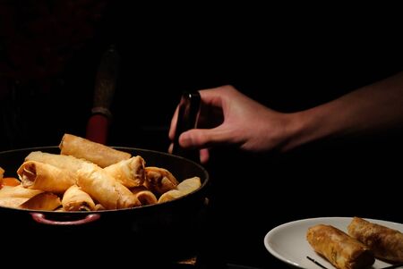 deep fried spring rolls  surve on the pan in dark background with hand pick up one of them and put in to small dishの写真素材