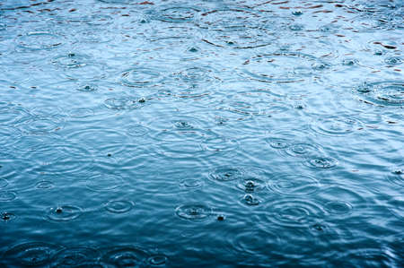 rain drops on the surface of water in a puddle with graduated shade of black shadow and reflection of blue skyの写真素材
