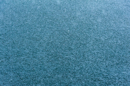 rain drops on the surface of water in a puddle with graduated shade of black shadow and reflection of blue skyの写真素材