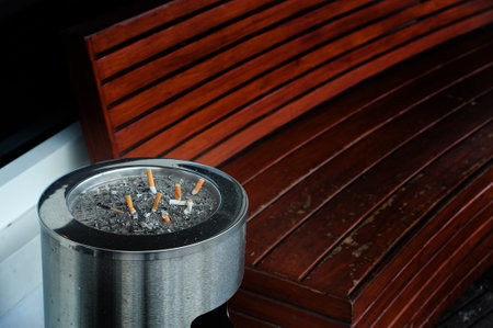 many cigarette stubs in the ashtyay near red bench at smoking areaの写真素材
