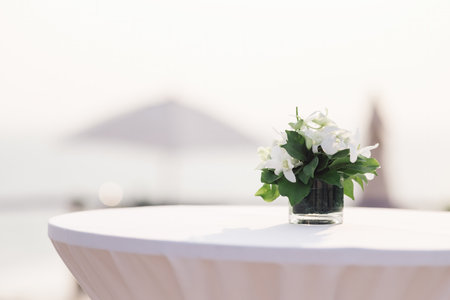 a glass vase with flowers on the white reception table at beachfront weddings party evenの写真素材