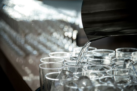 pouring cool pure transparent clear drinking water from the jar to clean glasses on the tableの写真素材
