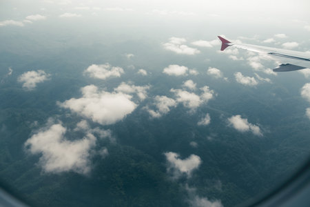 a view from airplane show hazy green hills cover by clouds with a wing of aircraft