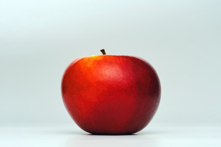 a fresh red apple isolated in graduated white background with back lighting and some dark shade of shadowの写真素材