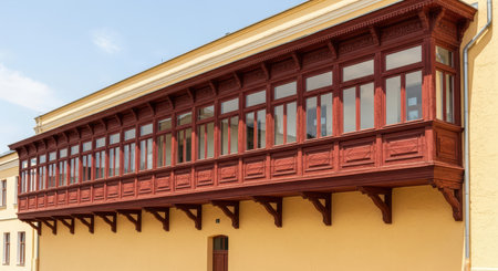 Historic red wooden balcony on yellow building exterior in sunny dayの素材