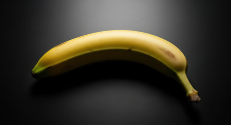 Perfectly ripe banana on dark surface with subtle lightingの素材