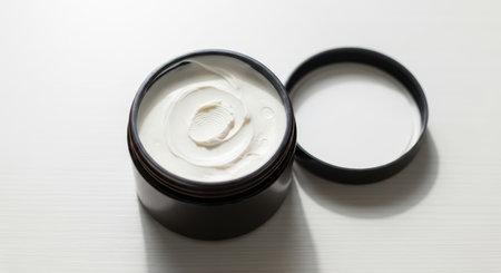 Open jar of moisturizing cream on white surface with lid removedの素材