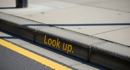 Urban street curb with yellow look up signの素材