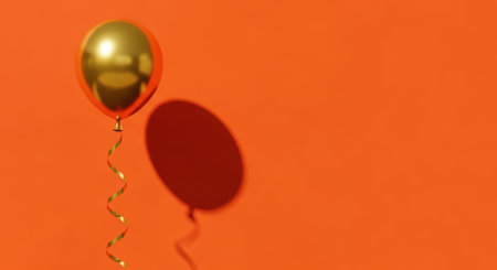 Golden balloon with spiral ribbon against orange backgroundの素材