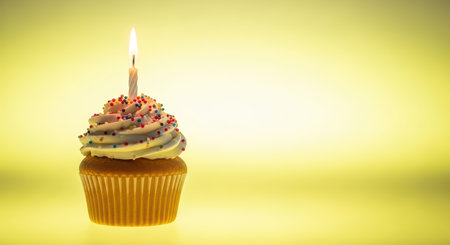 Festive cupcake with candle and sprinkles on yellow backgroundの素材