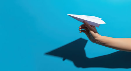 Hand holding paper airplane against blue sky backgroundの素材