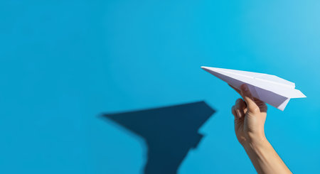 Hand holding paper airplane against bright blue sky backgroundの素材