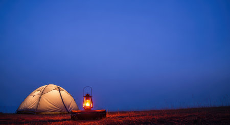Illuminated tent and lantern at dusk in open fieldの素材