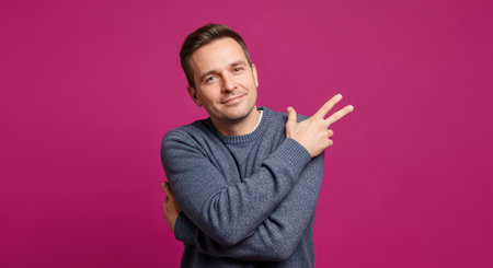 Confident young caucasian male in casual sweater against a vibrant pink backgroundの素材