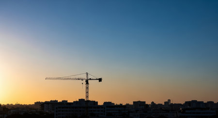 Construction crane silhouette against vibrant urban sunset skylineの素材