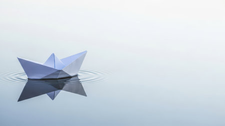 Minimalist paper boat floating on calm water surface with gentle ripplesの素材