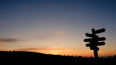 Silhouette of signpost against vibrant sunset sky in forest landscape.の素材