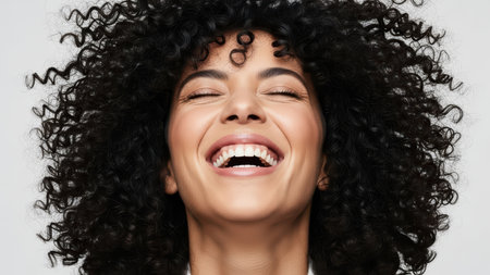 Joyful young woman with curly hair laughing joyously against white background.の素材
