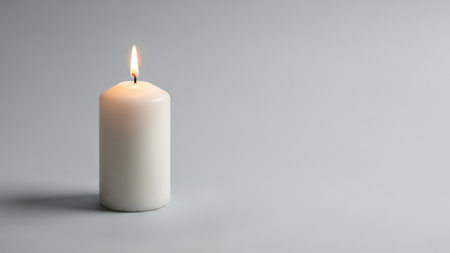 Simple white candle burning against minimalist gray background.の素材