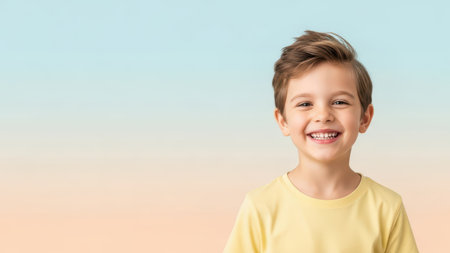 Young caucasian boy smiling in yellow shirt against pastel background.の素材