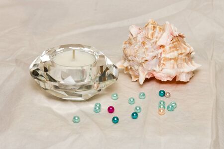 A composition of sea shelf, canddle and colourful pearls on a white backgroundの写真素材