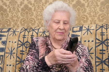 Senior woman dials the phone sitting on the sofa