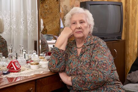 Portrait of senior caucasian woman with white hair about ninety years old sitting near the mirror in her bed roomの写真素材
