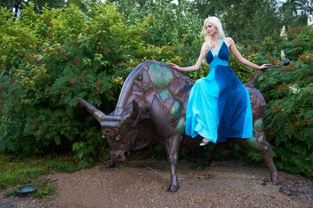 Blonde girl sits on the metal bull in the park