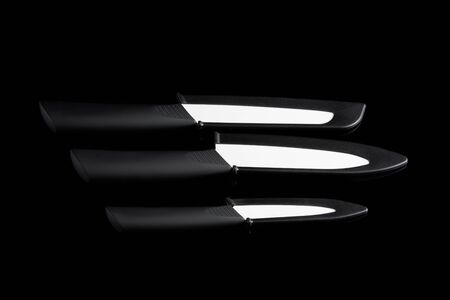Set of three ceramic knives in black cover on black reflecting backgroundの写真素材