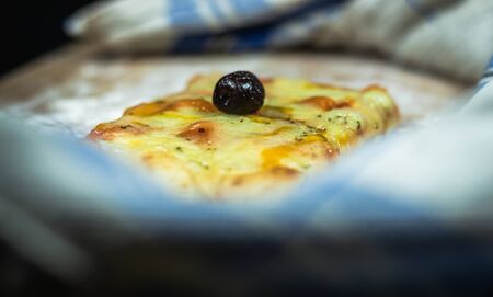 Flat bread pizza by cheese and black olives on a cutting board with flour Surrounded by a napkin in black backgroundの写真素材
