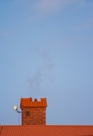 Red chimney with bricks, roof and sky backgroundの写真素材