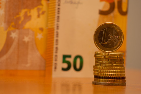 Close up of stacked coins and 1 euro on top, banknote in the backgroundの写真素材