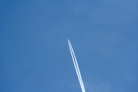 plane streak in the sky. Flying plane on the blue sky leaving behind white smokeの写真素材